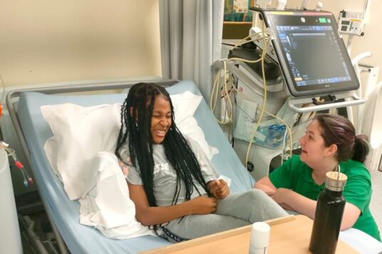 Neriya in her hospital bed with one of the St George's play specialists