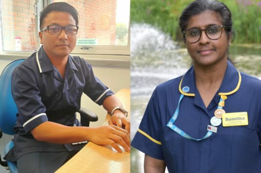 Mark Mencias on the left wearing a blue nurse uniform and sitting at a desk with Sumitha Janaky standing while wearing her blue nurse uniform