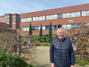 Martin Tyler wears a blue padded jacket and stands in front of St George's Hospital