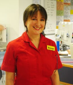 Breege wears a red uniform with a name badge