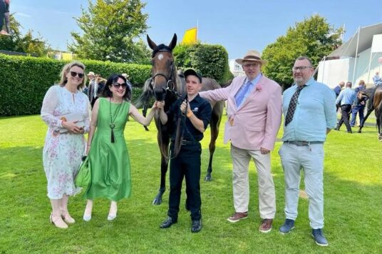 Four people at the races with a horse in the middle