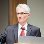 Sir Mark Lowcock in a grey suit, white shirt and red tie