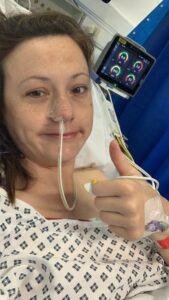 Harriet sitting in a hospital bed and gives the thumbs up